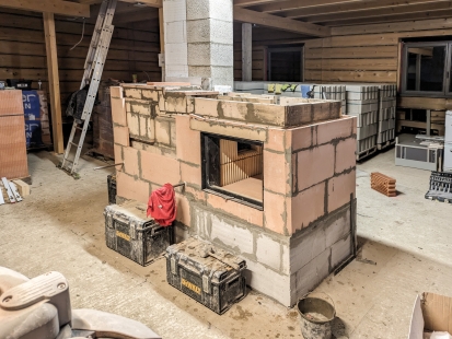 Těžká akumulační kamna s hliněnou omítkou jako dominantní prvek srubu - Stavba šamotových kamen. Jako tradiční kamnářských materiál je zde použita hliněná malta jako pojivo šamotových tvarovek topeniště a pro umístění absorbéru.  - foto: Kamnářství Křivonožka